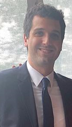 A brown haired man in a dark suit and tie. Business proper.