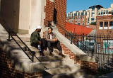 Two men sit and chat on steps outside a municipal building.