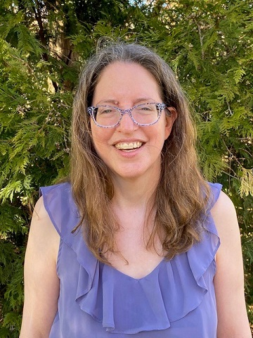 A long haired woman with glasses, smiling at the camera.