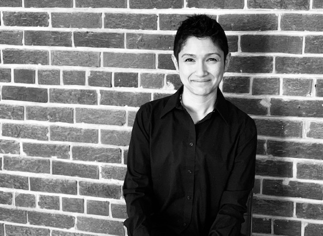 Black and white photo of a woman standing against a brick wall