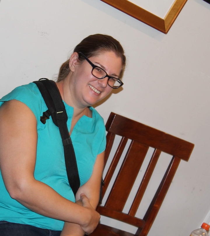 A woman with thick framed glasses and a teal shirt, smiling.