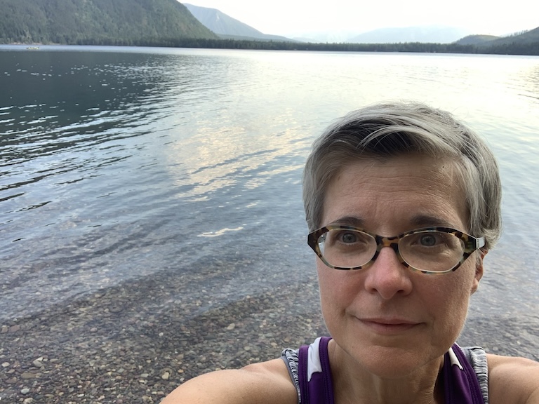 Selfie of woman with glasses in front of a crystal clear lake.